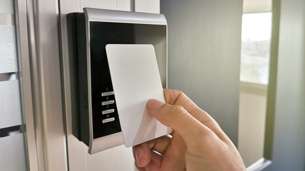 A hand is holding a white access card up to a card reader on a door.